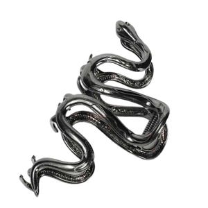 May include: A dark gray metal snake-shaped cuff bracelet. The bracelet coils around itself, with the head and tail of the snake visible. The design is detailed, with textured scales and a sleek, polished finish. The jewelry is set against a white background.
