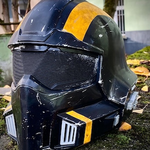 Könnte beinhalten: Ein schwarz-gelber Helm mit einem Mesh-Visier. Der Helm hat gelbe Streifen und ein verwittertes Aussehen. Das Design deutet auf ein futuristisches oder Science-Fiction-Thema hin, möglicherweise für Cosplay oder Ausstellungen.