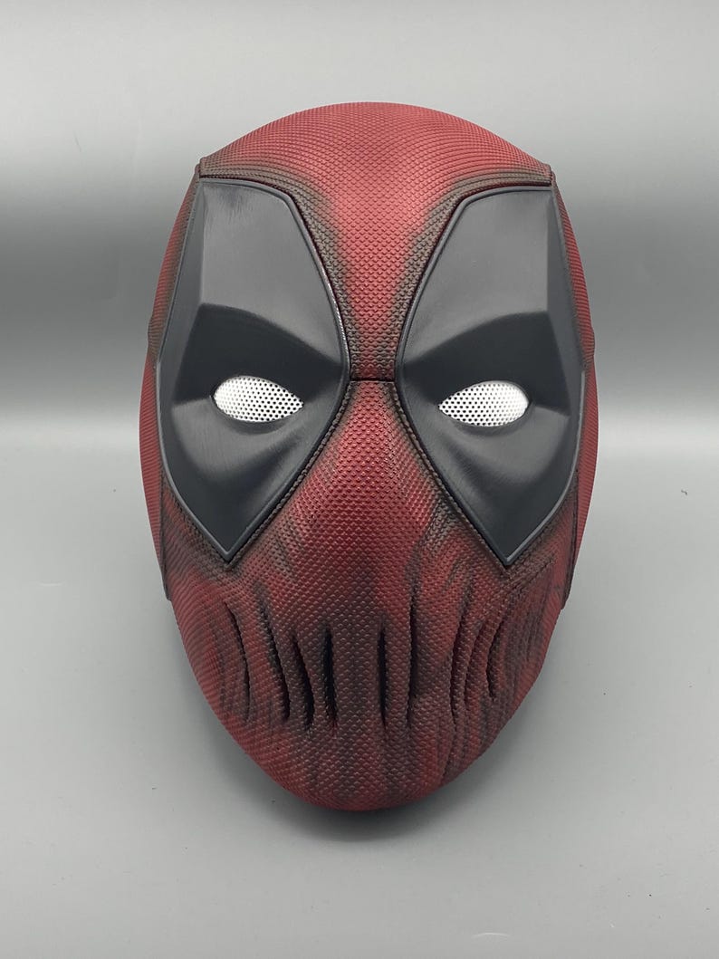 Puede incluir: Una m&aacute;scara de Deadpool roja y negra con una superficie texturizada. La m&aacute;scara tiene un &aacute;rea de ojos negra con ojos de malla blanca.