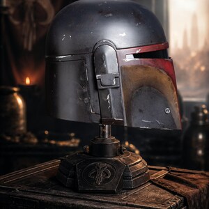 Peut inclure: Casque Mandalorien gris fonc&eacute; vieilli avec des accents rouges et jaunes, pr&eacute;sent&eacute; sur un socle d&eacute;taill&eacute;. Le casque pr&eacute;sente une visi&egrave;re en forme de T distinctive et est un objet de collection de l'univers Star Wars.
