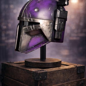 Peut inclure: Casque violet et argent&eacute;, probablement pour le cosplay ou l'exposition, mont&eacute; sur un support noir au-dessus d'une bo&icirc;te en bois. Le casque a un aspect vieilli avec des rayures et des accents m&eacute;talliques. L'arri&egrave;re-plan est flou.