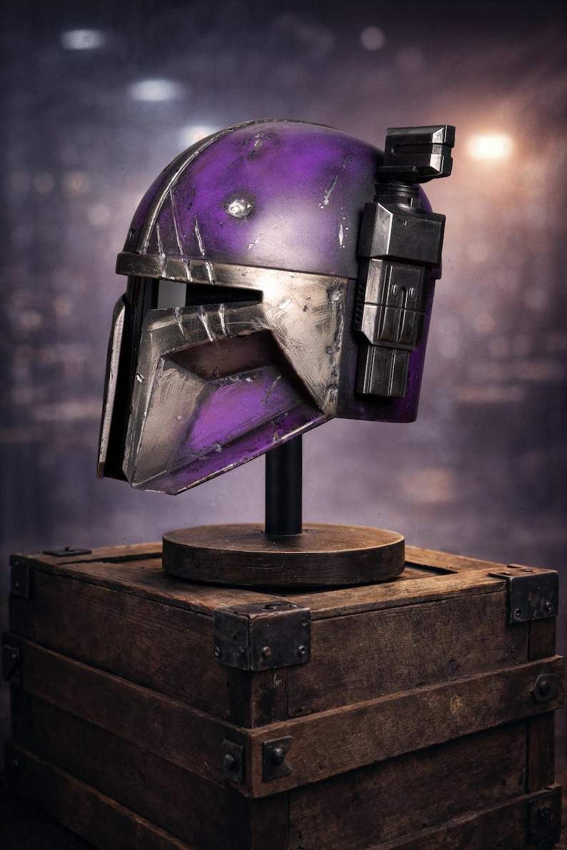 Peut inclure: Casque violet et argent&eacute;, probablement pour le cosplay ou l'exposition, mont&eacute; sur un support noir au-dessus d'une bo&icirc;te en bois. Le casque a un aspect vieilli avec des rayures et des accents m&eacute;talliques. L'arri&egrave;re-plan est flou.