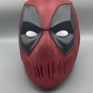Puede incluir: Una m&aacute;scara de Deadpool roja y negra con una superficie texturizada. La m&aacute;scara tiene un &aacute;rea de ojos negra con una malla blanca que cubre los ojos.