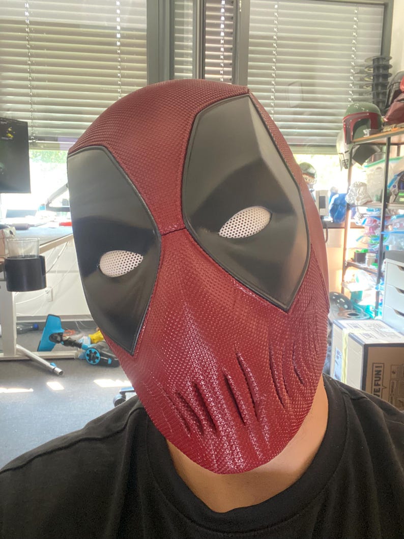 Puede incluir: Una m&aacute;scara de Deadpool roja y negra con una superficie texturizada. La m&aacute;scara tiene un &aacute;rea de ojos negra con ojos de malla blanca.