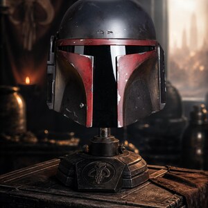 Peut inclure: Casque de r&eacute;plique d&eacute;taill&eacute;, avec un d&ocirc;me noir, des accents rouges et une visi&egrave;re en forme de T. Mont&eacute; sur un support m&eacute;tallique avec un symbole. L'ensemble sugg&egrave;re un th&egrave;me de science-fiction ou de fantaisie.