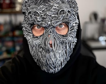May include: A person wearing a black hoodie with a detailed, gray skull mask. The mask is made of many skulls and has a textured, 3D design.