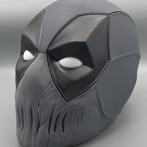 Puede incluir: Una m&aacute;scara de Deadpool gris con una superficie texturizada y una m&aacute;scara para los ojos negra. La m&aacute;scara tiene un dise&ntilde;o detallado con una mand&iacute;bula afilada y una nariz en relieve.