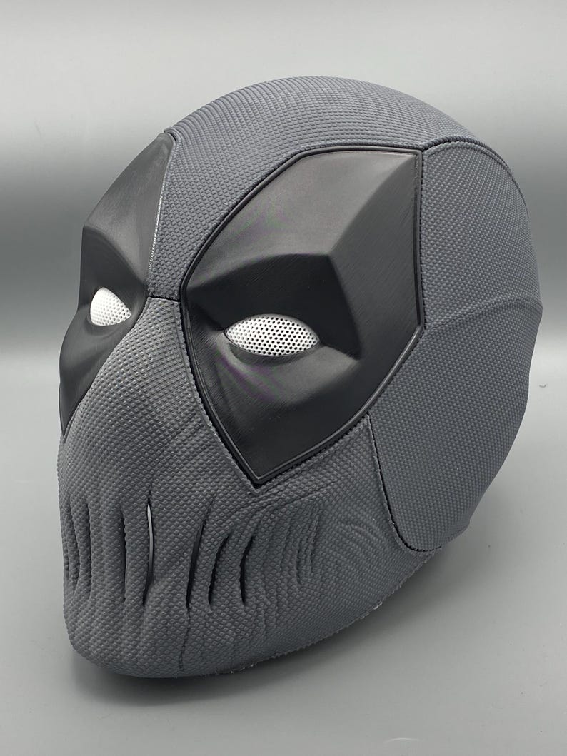 Puede incluir: Una m&aacute;scara de Deadpool gris con una superficie texturizada y una m&aacute;scara para los ojos negra. La m&aacute;scara tiene un dise&ntilde;o detallado con una mand&iacute;bula afilada y una nariz en relieve.