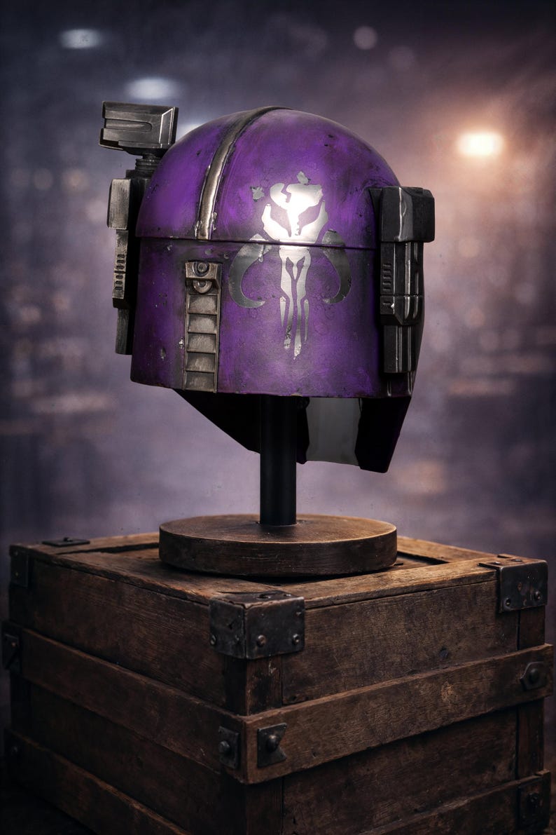 Peut inclure: Un casque violet avec des d&eacute;tails argent&eacute;s et un embl&egrave;me blanc, pr&eacute;sent&eacute; sur un support en bois sur une bo&icirc;te en bois. Le casque a un aspect vieilli, probablement un accessoire ou un objet de collection.