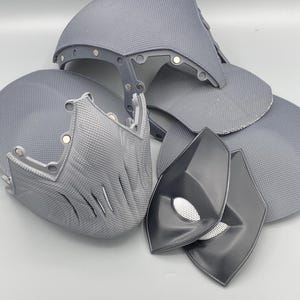 Puede incluir: Un conjunto de piezas de disfraz impresas en 3D de color gris, que incluyen una m&aacute;scara, un casco y dos piezas para los ojos. Las piezas est&aacute;n hechas de un material pl&aacute;stico texturizado.