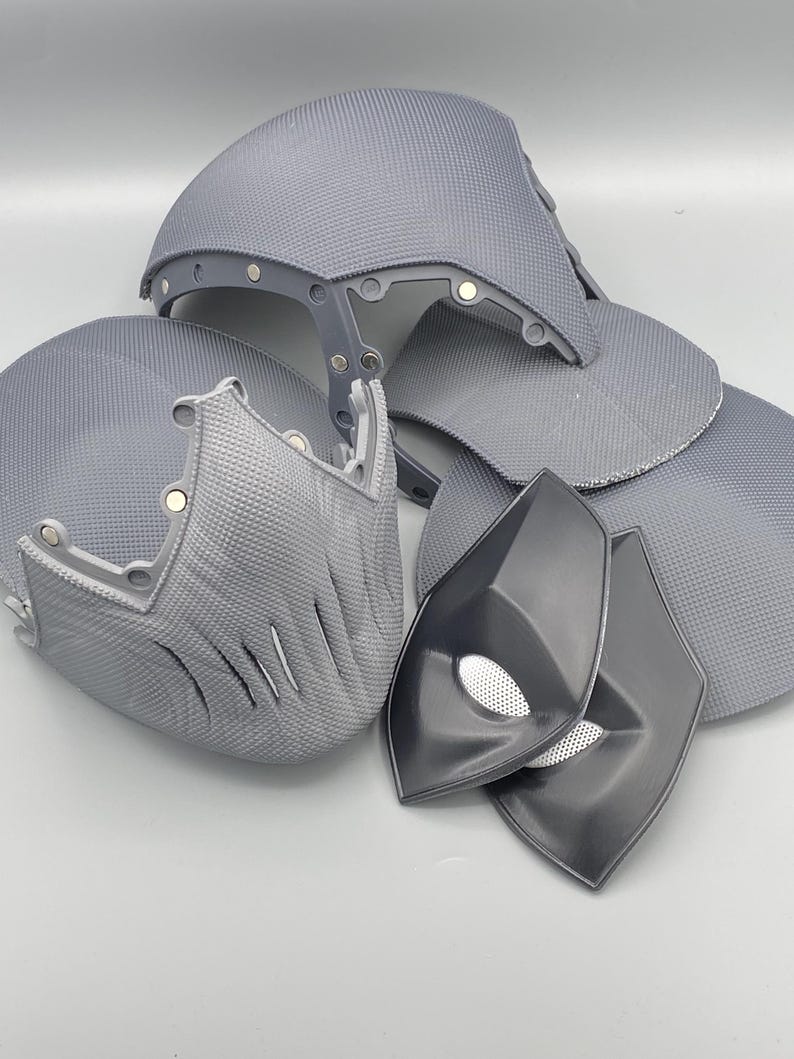 Puede incluir: Un conjunto de piezas de disfraz impresas en 3D de color gris, que incluyen una m&aacute;scara, un casco y dos piezas para los ojos. Las piezas est&aacute;n hechas de un material pl&aacute;stico texturizado.