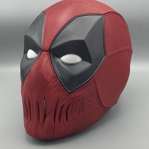Puede incluir: Una m&aacute;scara de Deadpool roja y negra con una superficie texturizada y una cubierta de malla para los ojos.