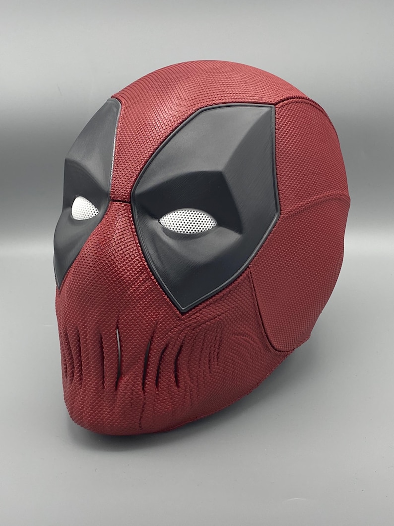 Puede incluir: Una m&aacute;scara de Deadpool roja y negra con una superficie texturizada y una cubierta de malla para los ojos.