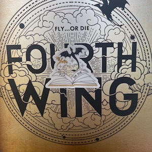 K&ouml;nnte beinhalten: Ein Buchcover mit einem schwarzen und goldenen Design, das die Worte "Fourth Wing" und einen Drachen zeigt. Das Buchcover hat einen Aufkleber mit einem Drachen und den Worten "Fly...or Die" darauf.