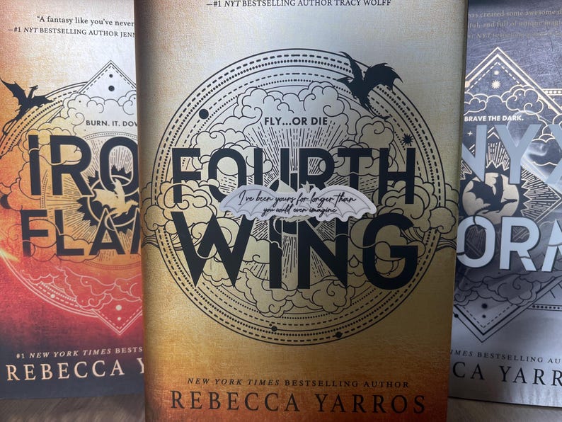 May include: Three fantasy novels with black and white illustrations of dragons and clouds. The titles are "Iron Flame", "Fourth Wing", and "Nyx & Ora". All three books are by the author Rebecca Yarros.