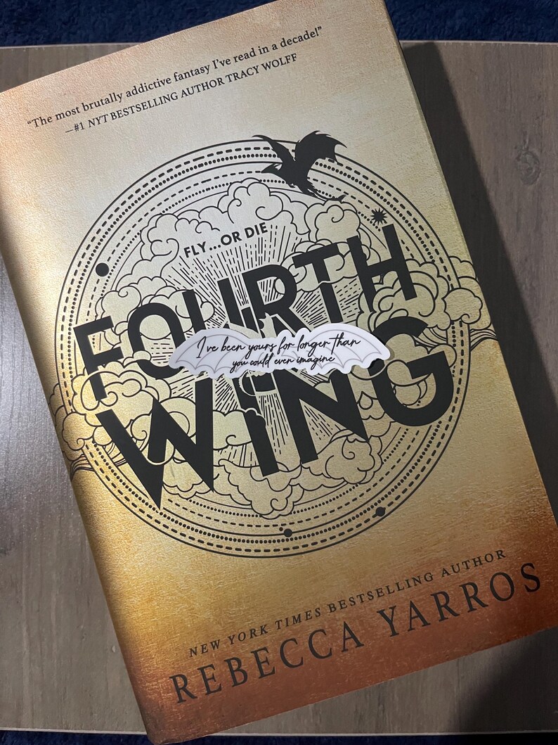 May include: A book cover with a gold background and black text. The title is "Fourth Wing" with the words "Fly...or Die" above it. The author's name is "Rebecca Yarros" and the text "New York Times Bestselling Author" is below it. The book cover features a black dragon with a white wing.
