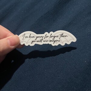 May include: White sticker with black text and a pair of bat wings. The text reads "I've been yours for longer than you could even imagine."
