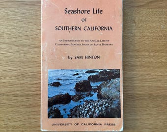 Może przedstawiać: Książka w miękkiej oprawie zatytułowana Seashore Life of Southern California autorstwa Sama Hintona, z brzoskwiniową okładką, czarnym tekstem i prostokątnym zdjęciem ciemnych skał oraz niebieskiej wody morskiej, z nadrukowaną ceną 3,95 $.