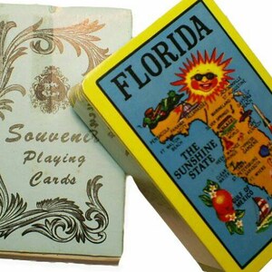 May include: A deck of playing cards with a blue and silver design on the box. The cards feature a map of Florida with the text "Florida, The Sunshine State".