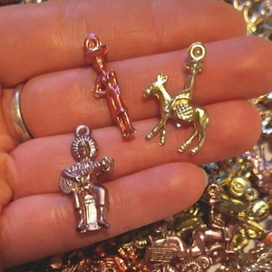 May include: A collection of gold, silver, and copper-toned metal charms featuring various figures, including a man playing a guitar, a camel, and a person standing. The charms are displayed on a hand.