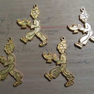 May include: Four gold-colored metal charms depicting a person carrying a lamp. Each charm is about 2 inches tall and features a detailed design.