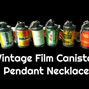 May include: A vintage film canister pendant necklace with six different film canisters. The canisters are all different colors and have different text on them. The necklace is made of a silver chain.