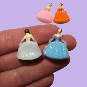 May include: Four plastic figurines of women wearing dresses. The dresses are pink, orange, white, and blue.