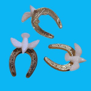 May include: Three gold-colored horseshoe-shaped charms with white dove accents. The charms are set against a bright blue background. One charm has the text "MADE IN HONG KONG".