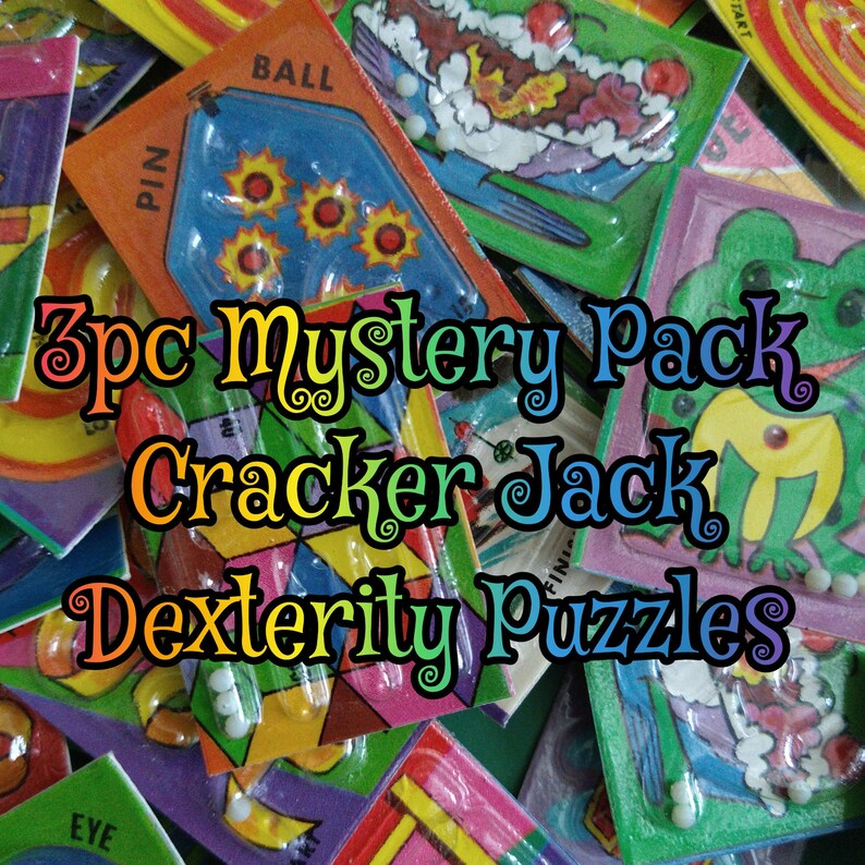 May include: A close-up of a 3pc Mystery Pack of Cracker Jack Dexterity Puzzles. The puzzles are colorful and feature various designs, including a frog, a ball, and a pin. The puzzles are made of plastic and have a clear plastic cover.