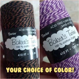 May include: Two spools of Darice Baker's Twine, one brown and black, the other purple and white. Both spools are 410 feet long and made of 100% cotton. The text on the label reads "Acid Free - Libre de Acide - Sans Acide".