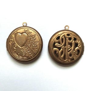May include: Two antique gold-colored lockets. One locket features a heart, flowers, and a decorative pattern. The other locket has an ornate, stylized monogram design. Both lockets have a small loop at the top for a chain.