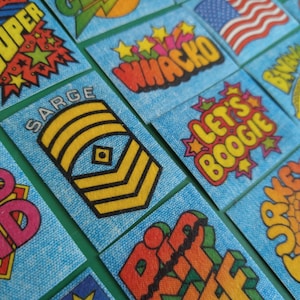 May include: A collection of colorful, illustrated patches with various phrases, including "Super", "Whacko", "Sarge", "Let's Boogie", "Turkey", and "Rip Off".