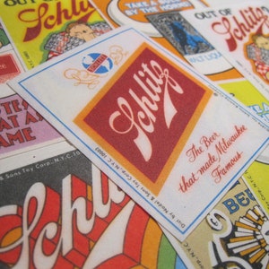 May include: Vintage Schlitz beer advertising stickers with red, white, and yellow colors. The stickers feature the Schlitz logo and the text "The Beer that made Milwaukee Famous".