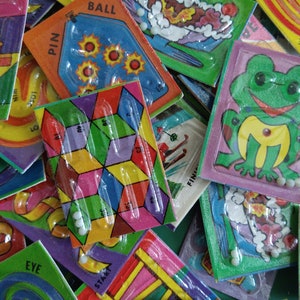 May include: A collection of colorful plastic maze games with different themes, including a frog, a ball, a pin, and a bull's eye. Each game has a clear plastic cover and a small white marble to move through the maze.