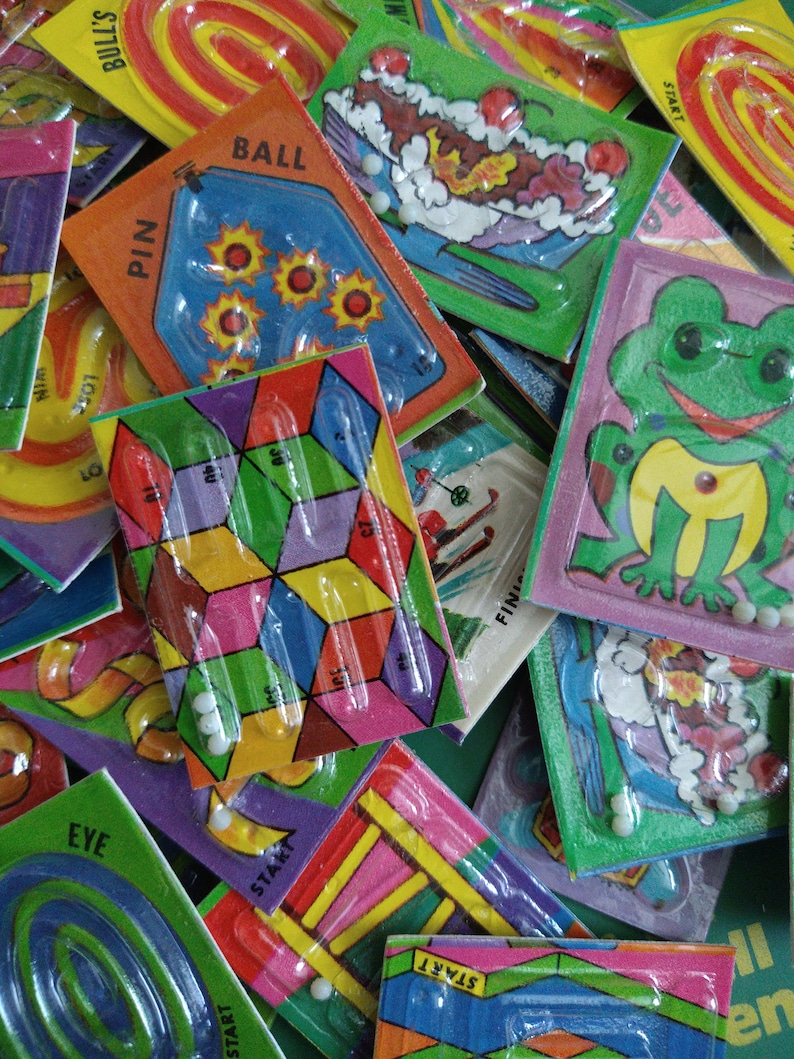 May include: A collection of colorful plastic maze games with different themes, including a frog, a ball, a pin, and a bull's eye. Each game has a clear plastic cover and a small white marble to move through the maze.
