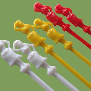 May include: A collection of colorful cocktail stirrers. The stirrers feature a woman-shaped design in white, yellow, and red. The background is a solid green color. These decorative stirrers are ideal for parties and events.