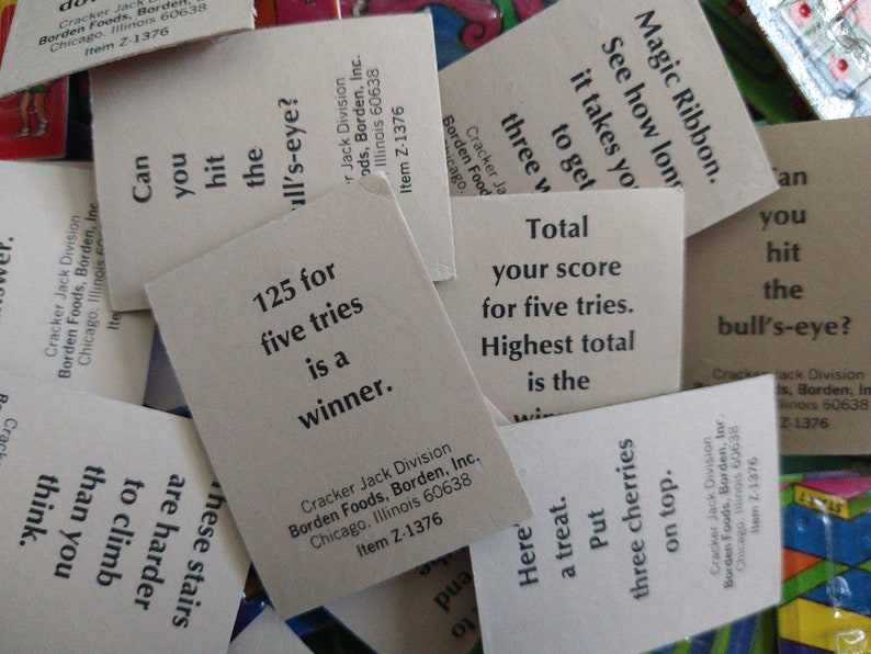 May include: A close-up of several white cards with black text. The cards are from a Cracker Jack game and have instructions for playing the game. The text on the cards includes "125 for five tries is a winner", "Total your score for five tries. Highest total is the winner", "Can you hit the bull's-eye?", and "Here's a treat. Put three cherries on top."