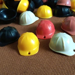 May include: Assortment of colorful hard hats in various colors including yellow, red, white, and black. The hard hats are made of plastic and have a smooth finish.