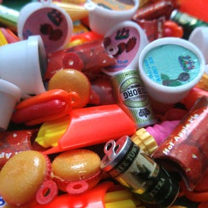 May include: A collection of colorful plastic charms, including a hot dog, hamburger, ice cream cone, and a can of beer. The charms are all in the shape of food items and have a retro look.