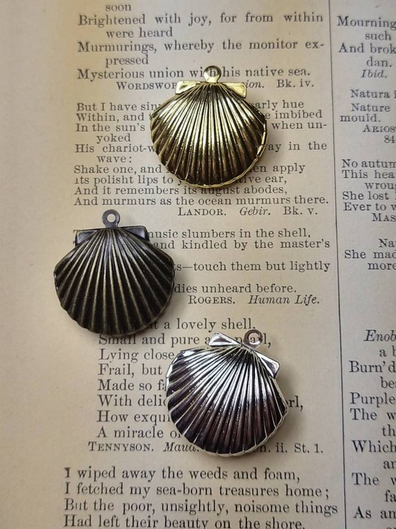 May include: Three seashell pendants in gold, bronze, and silver tones rest on a vintage book page. Each pendant features a detailed, ridged design, with a small loop for attaching to a chain or cord. The pendants are ideal for jewelry making.
