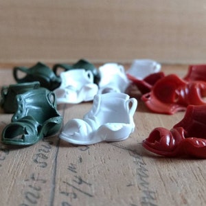 May include: A collection of plastic toy sandals in green, white, and red. The sandals are in various styles and have a gladiator-style design.