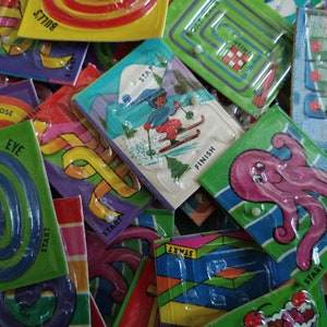 May include: A collection of colorful plastic maze games with different themes, including a skier, an octopus, and a bull's eye. Each game has a start and finish point and a small white bead to move through the maze.