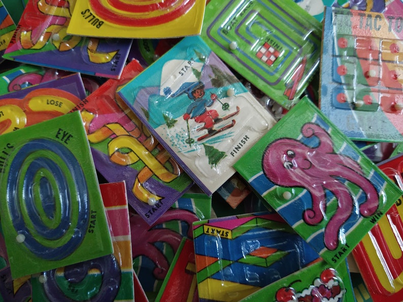 May include: A collection of colorful plastic maze games with different themes, including a skier, an octopus, and a bull's eye. Each game has a start and finish point and a small white bead to move through the maze.