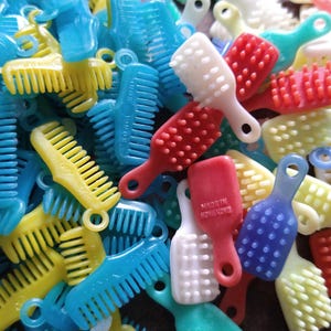 May include: A collection of small, colorful plastic combs and brushes in various shades of blue, yellow, red, and white. Some brushes have a handle and a textured surface. The combs have teeth and a small hole for hanging.