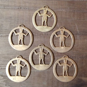 May include: Six gold-colored metal ornaments with a cutout design of a person in a suit. The ornaments are round and have a hole at the top for hanging.