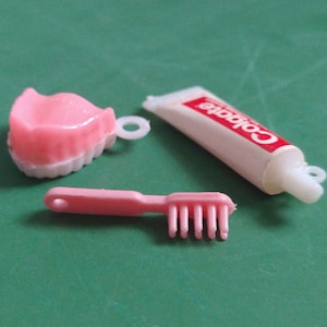 May include: A pink plastic toothbrush, a pink plastic set of dentures, and a white tube of Colgate toothpaste.