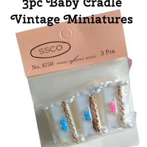 May include: Three white miniature baby cradles with gold trim and blue and pink accents. The cradles are packaged in a clear plastic bag with a pink and white label that reads "3pc Baby Cradle Vintage Miniatures" and "SSCO No. 8750 MADE IN HONG KONG 3 Pcs."