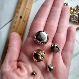 May include: A collection of silver and gold jingle bells of various sizes. The bells are in a person's hand.