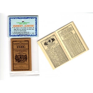 May include: A miniature 1853 edition of Farmer's Almanac. The cover is brown with black text and illustrations. The open pages show columns of text and numbers. A blue and white tag reads "Collector's Miniature" and "Farmer's Almanac."