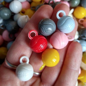 May include: A hand holding a variety of colorful plastic balls with different patterns. The balls have small loops for hanging. The colors include red, yellow, blue, pink, and gray.